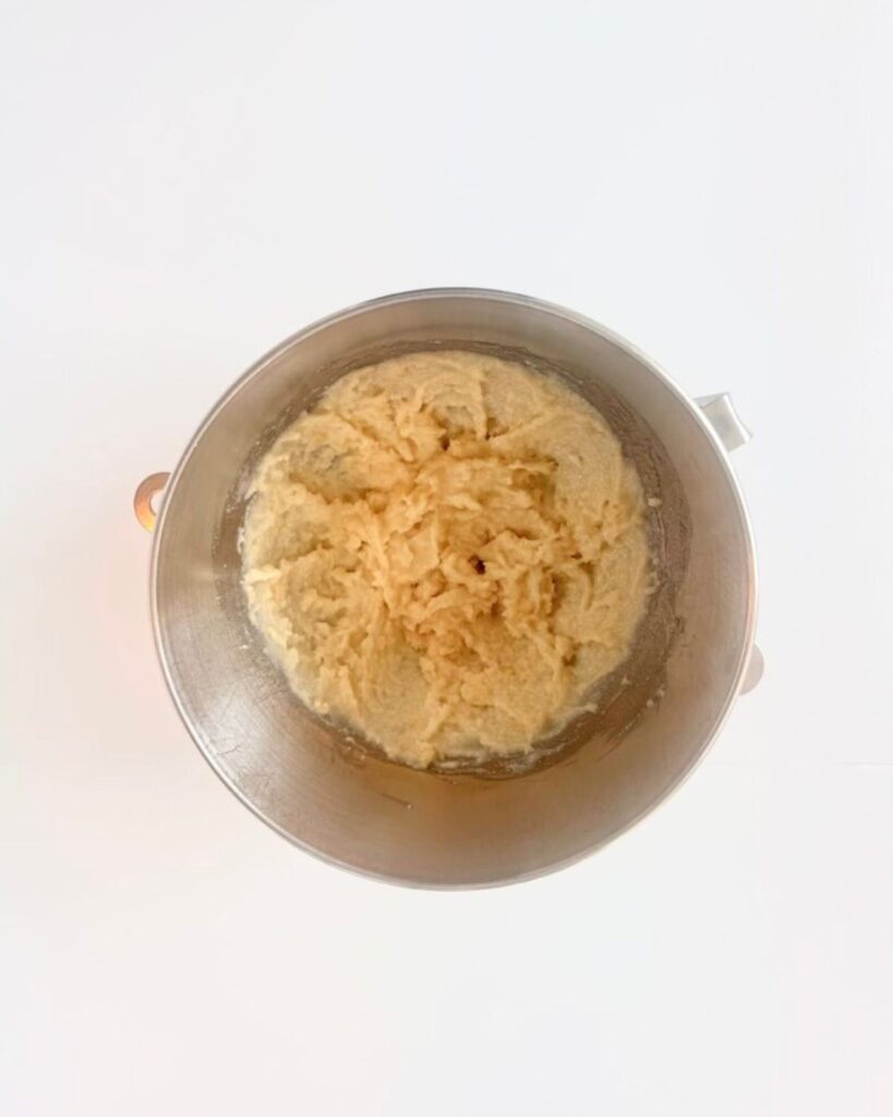 Almond paste, sugar, and egg whites beaten together into a pale, fluffy mixture in a mixing bowl.